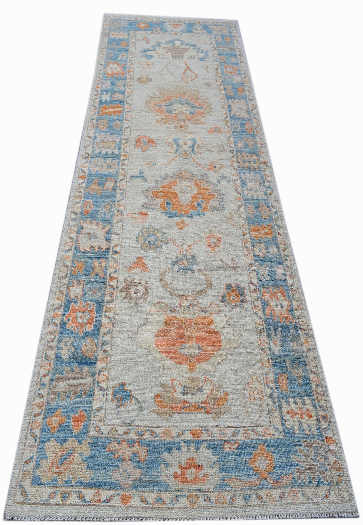 Transitional Oushak runner with blue and orange palmette motifs on a light grey field and a decorative border.