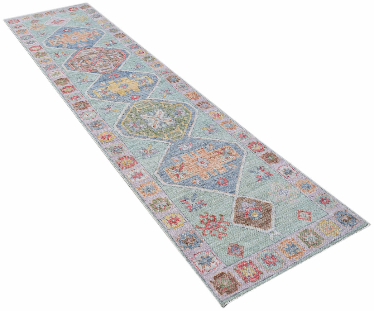 Transitional Oushak runner with a light green field, colourful floral medallions, and a decorative patterned border.