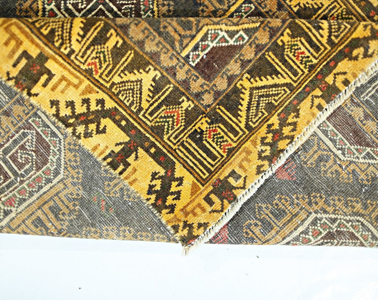 A folded vintage Afghan Baluch rug featuring intricate geometric patterns in brown and yellow tones.