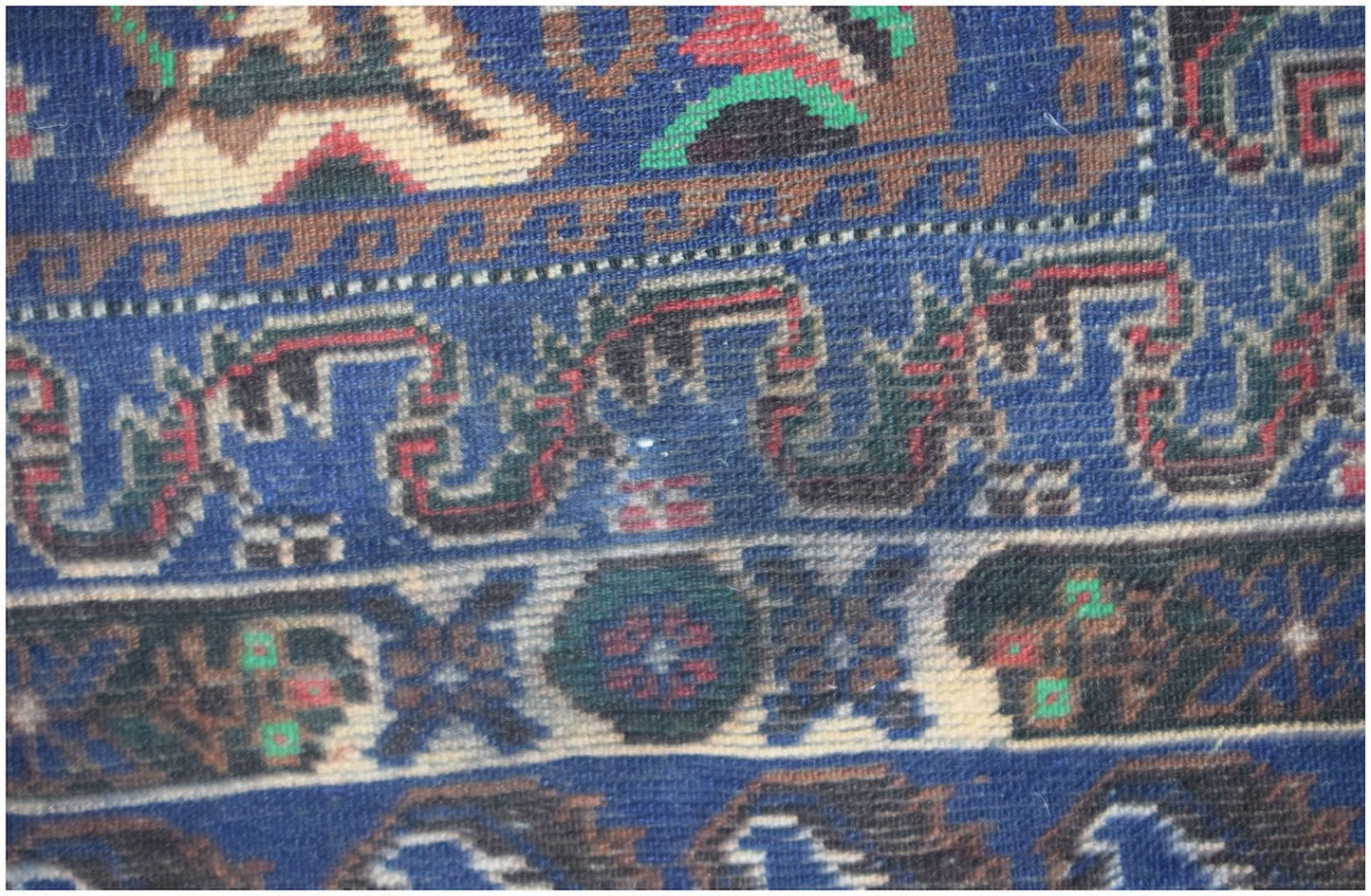 A close-up of a vintage Afghan Baluch rug featuring intricate geometric patterns in blue and red.