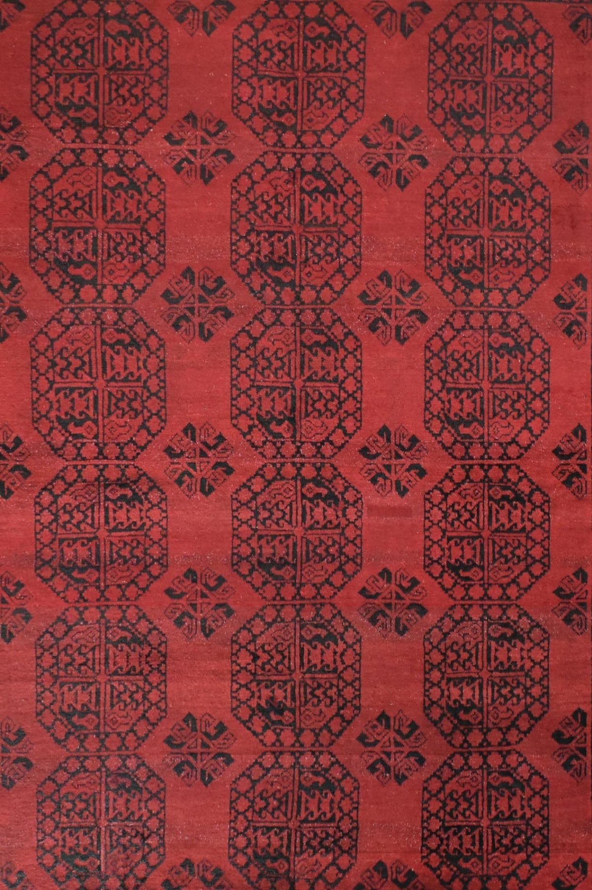 A vintage handmade Afghan Turkmen rug featuring a repeating geometric pattern in black on red.