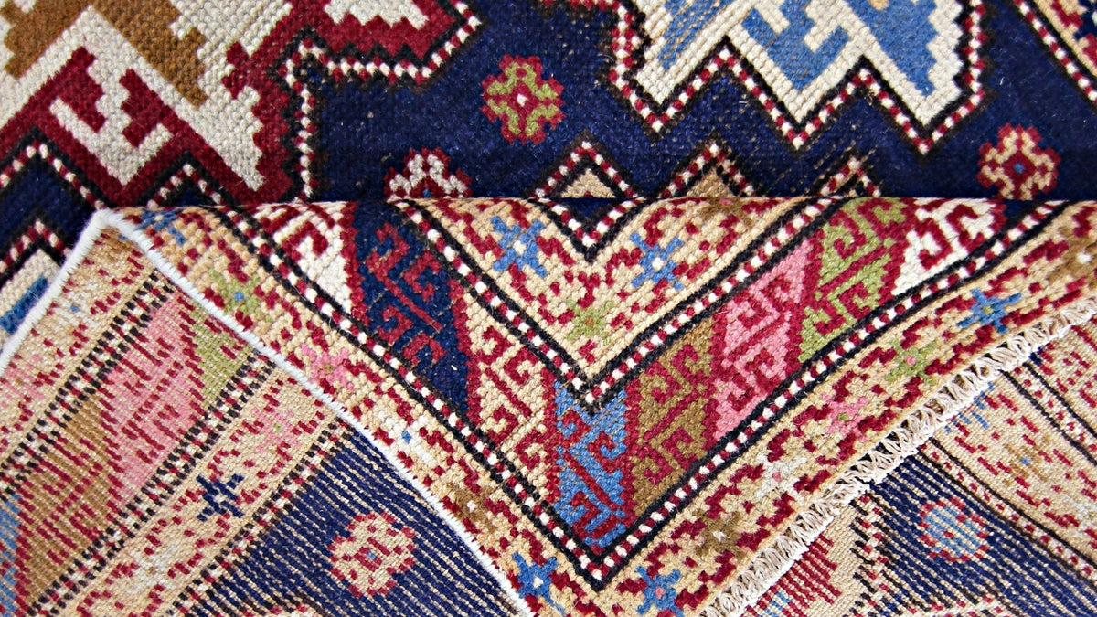 Close-up of a vintage Caucasian Kazak rug showing geometric medallions in red, blue, and gold with a visible wool pile.