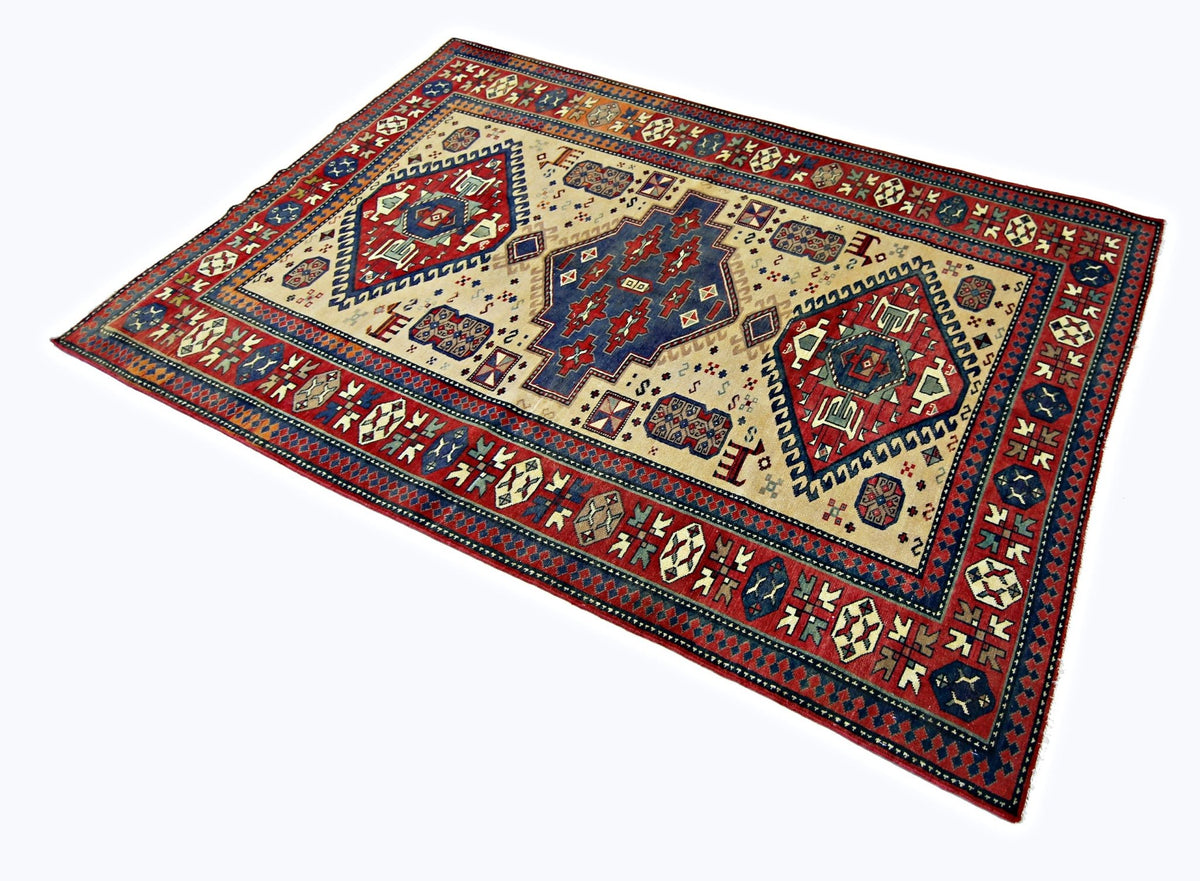 Vintage Caucasian Kazak rug with bold blue and red geometric medallions on a cream field and a patterned border.