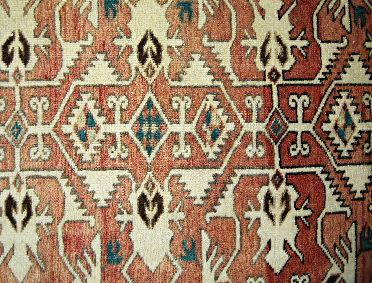 A vintage Persian rug featuring a geometric pattern in shades of red, cream, and teal.