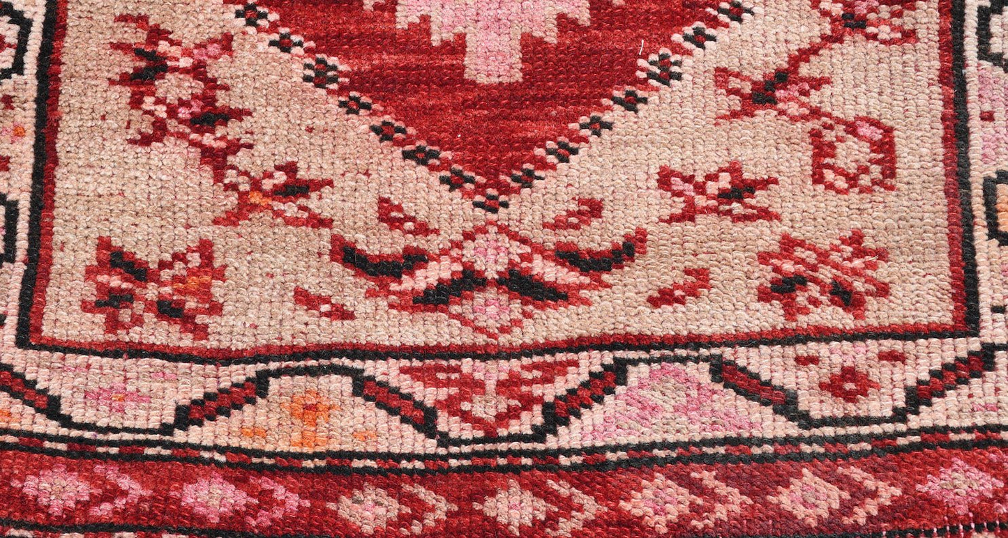 A vintage Kurdish Herki runner featuring tribal geometric motifs in red, pink, and beige wool.
