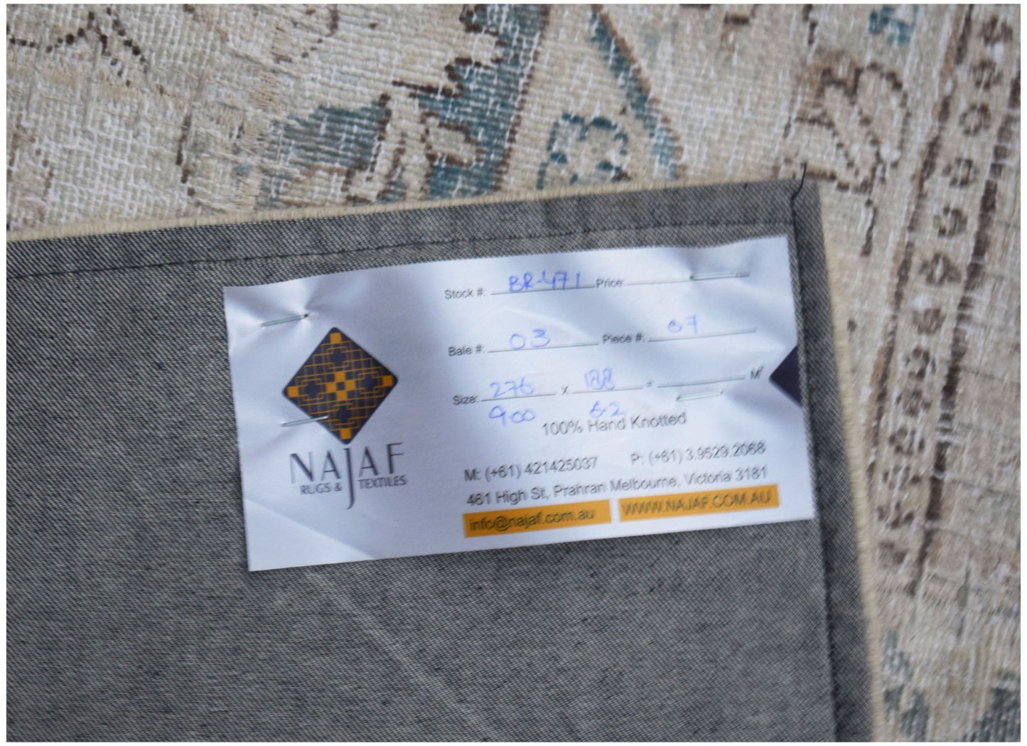 A vintage patchwork rug with a detailed pattern, shown from the back with a product label attached.