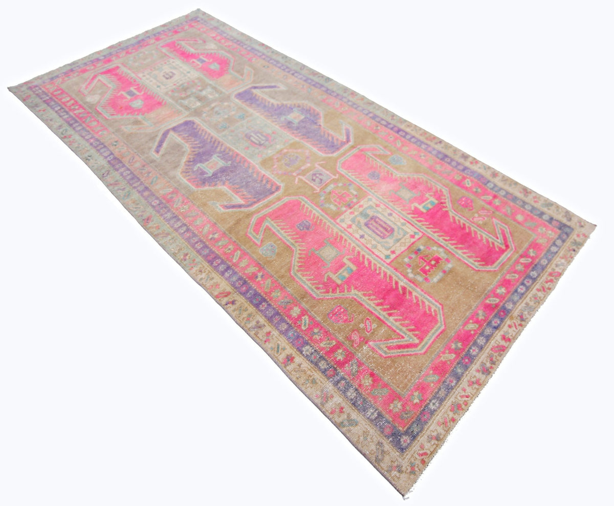 Vintage Persian Ardabil wool rug featuring faded pink and purple geometric medallions on a weathered tan field.