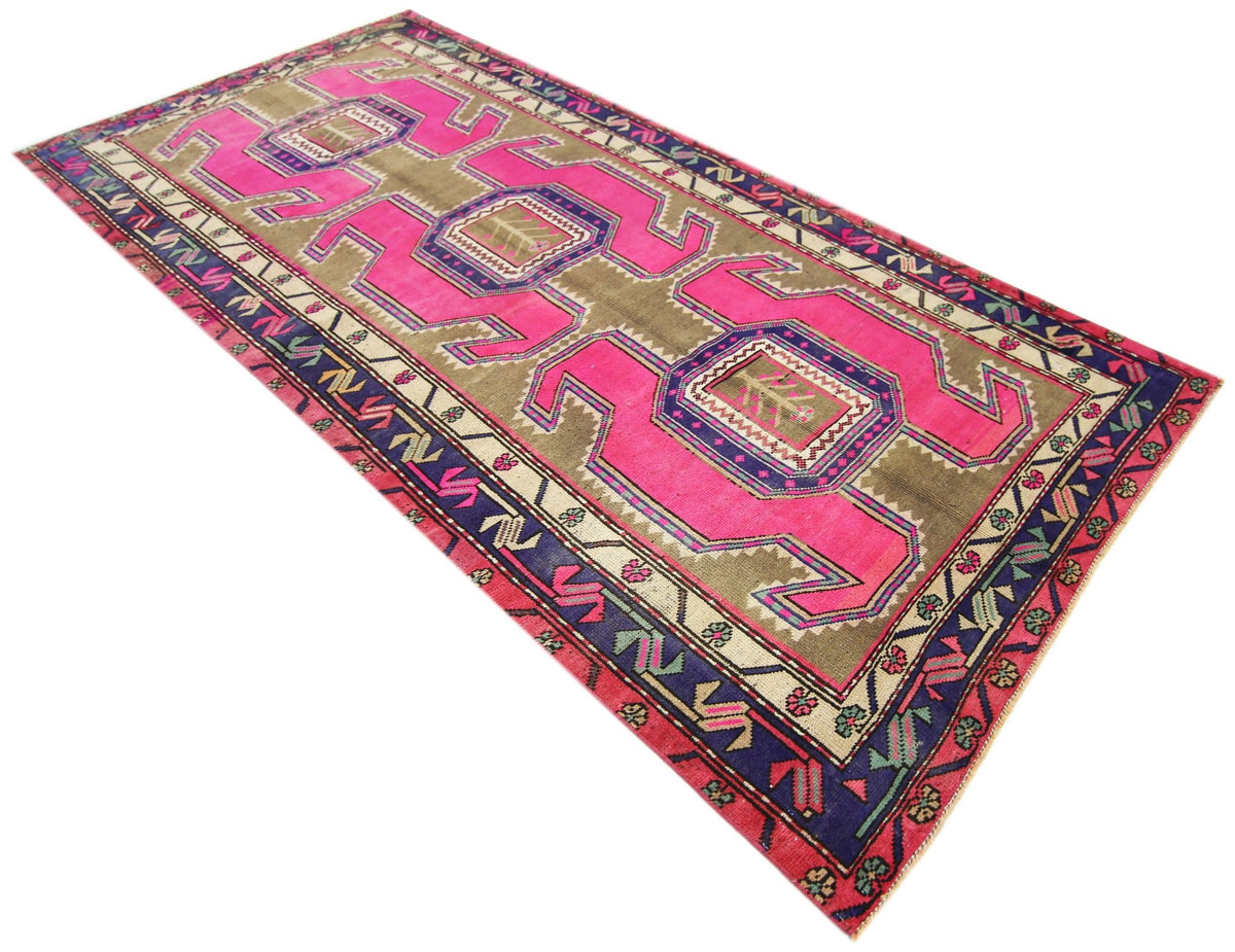 Vintage Persian Ardabil wool rug featuring bold pink medallions, geometric motifs, and a deep blue border on a muted brown field.