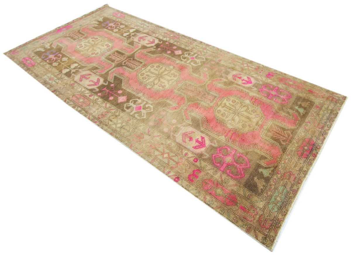 Vintage Persian Ardabil wool rug featuring faded brown and vibrant pink geometric medallions on a weathered pile.
