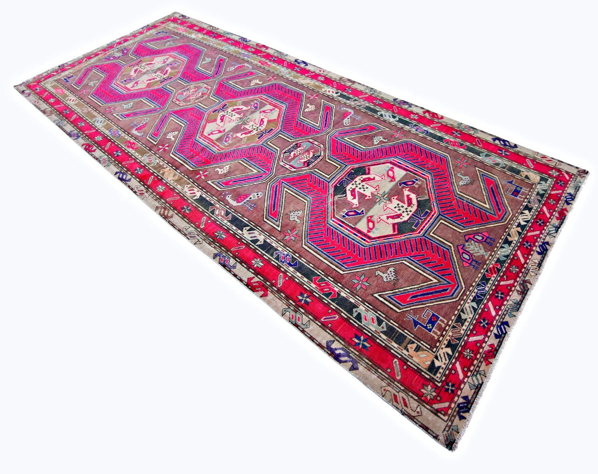 Vintage Persian Ardabil wool rug featuring vibrant pink geometric medallions, intricate animal motifs, and a faded brown field.