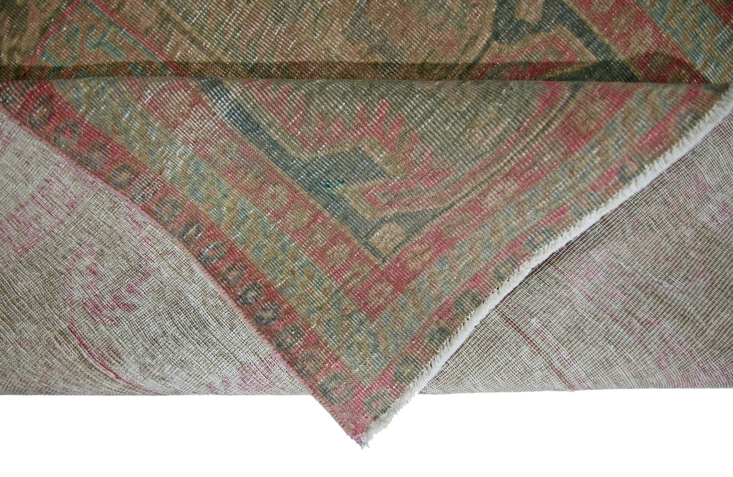 A corner of a vintage Persian Ardabil rug is folded back to show its wool pile and cotton base.
