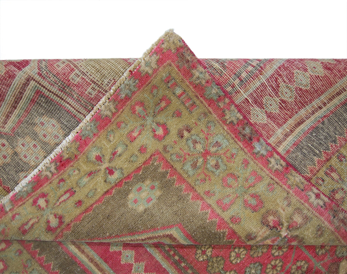 A vintage Persian Ardabil rug featuring a folded corner with intricate floral patterns in red and tan.