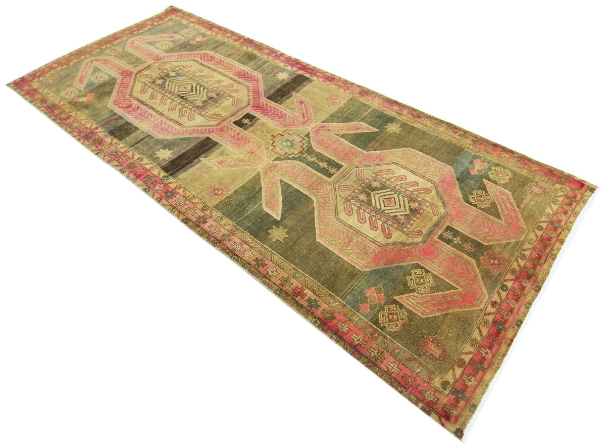 Vintage Persian Ardabil wool runner featuring geometric pink and olive green tribal motifs on a weathered, textured pile.