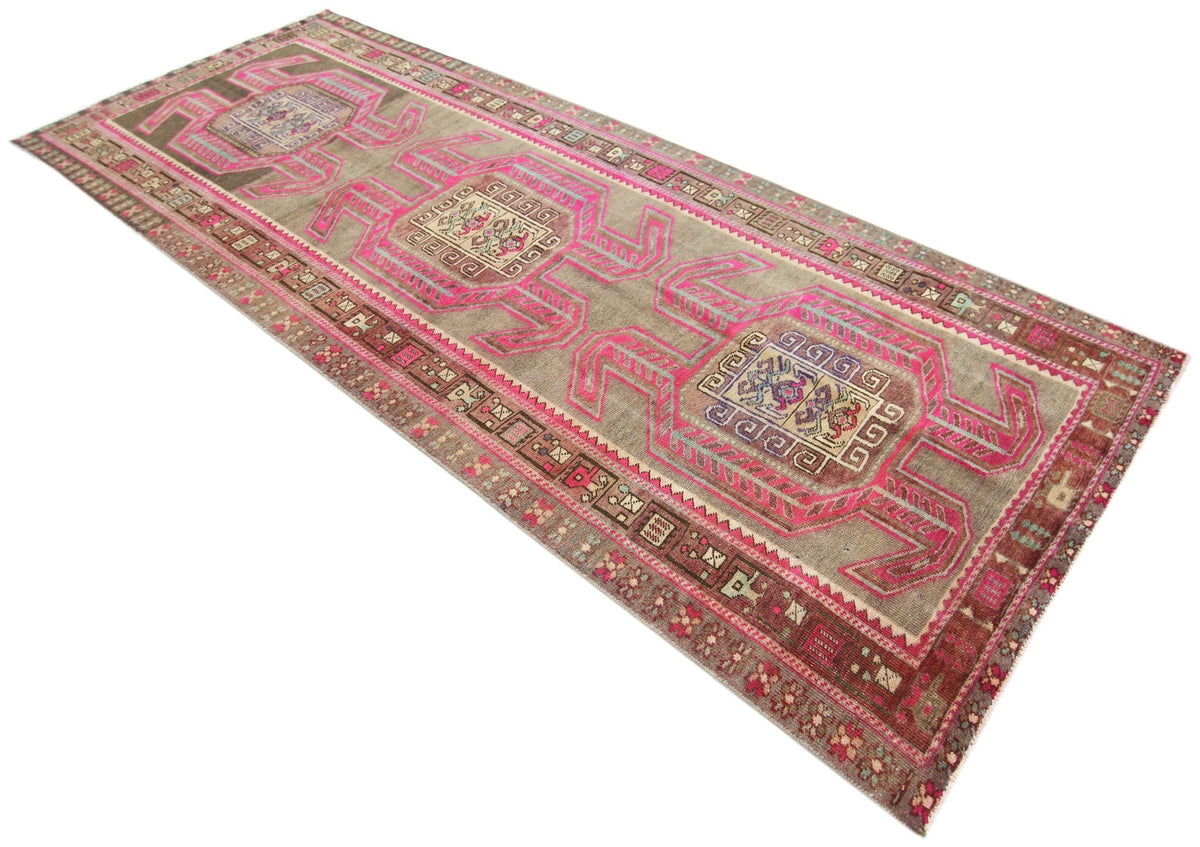 Vintage Persian Ardabil wool runner featuring geometric pink motifs and intricate borders on a weathered taupe background.