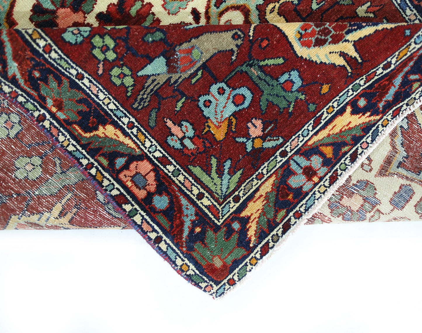 A folded vintage Persian Bakhtiari rug featuring intricate floral and bird motifs in rich colors.