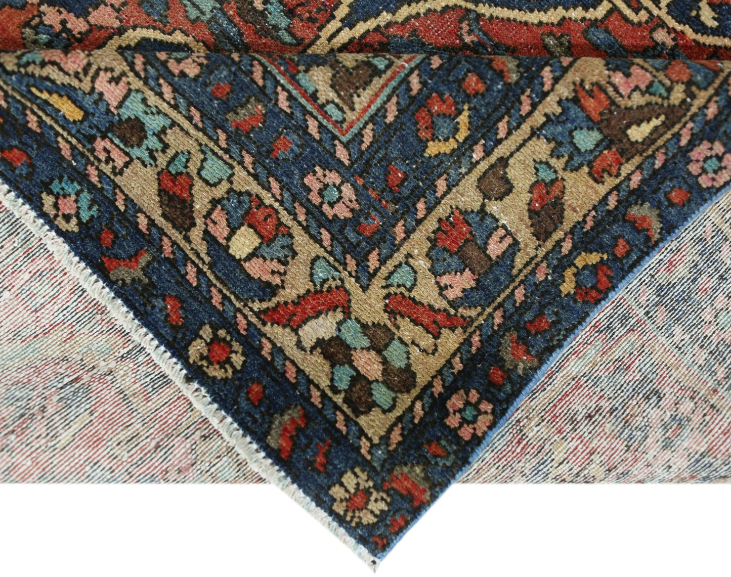 A corner of a vintage Persian Bakhtiari rug showing intricate floral patterns in blue and tan.