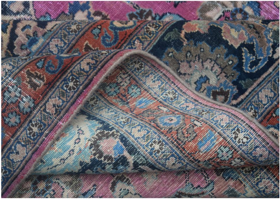 A folded vintage Persian Bidjar rug featuring intricate floral patterns in pink, blue, and red.