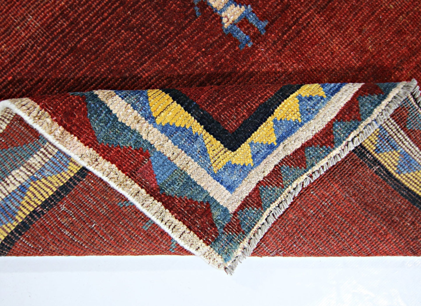 A vintage Persian Shiraz rug with a deep red field and a folded corner showing geometric patterns.