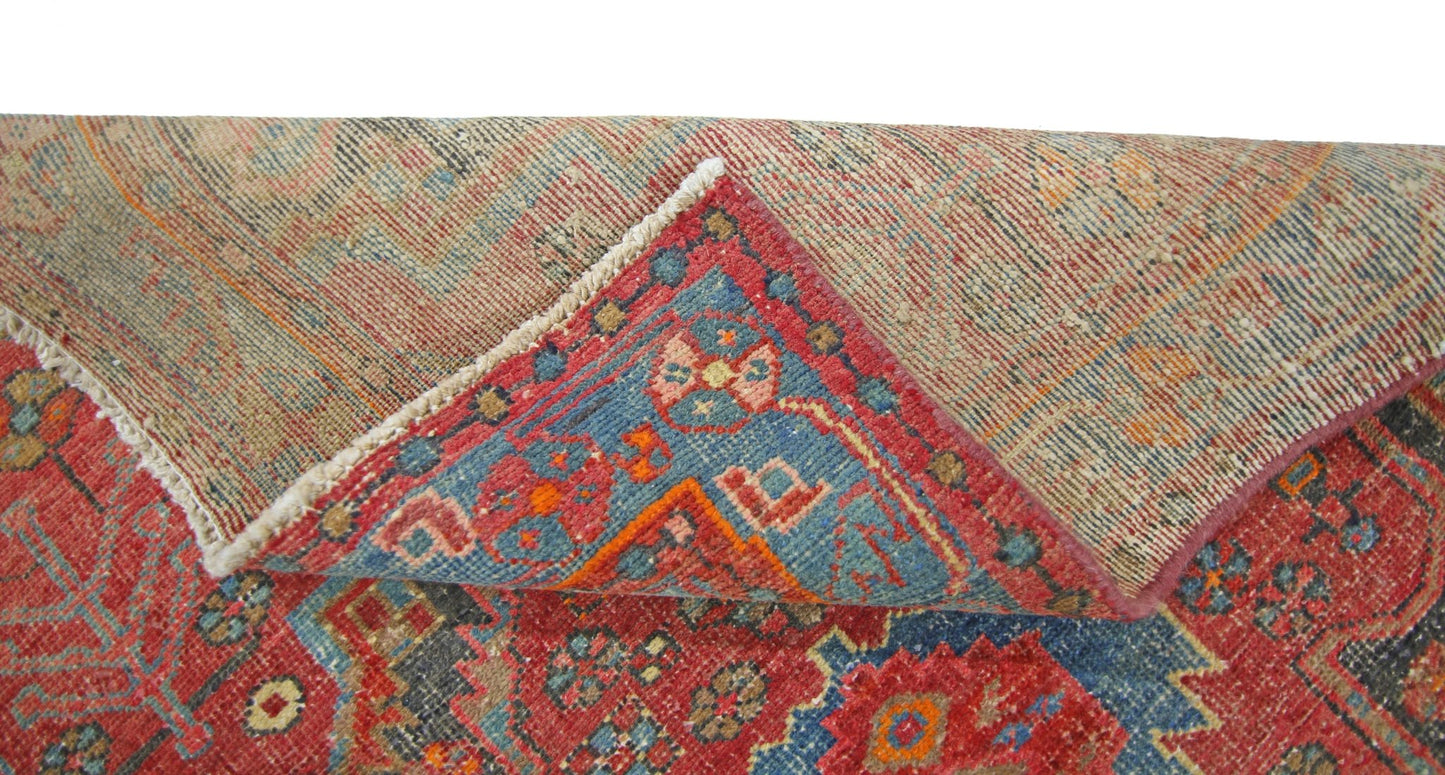 A corner of a vintage Persian Hamadan rug is folded back to reveal its wool pile and cotton base.