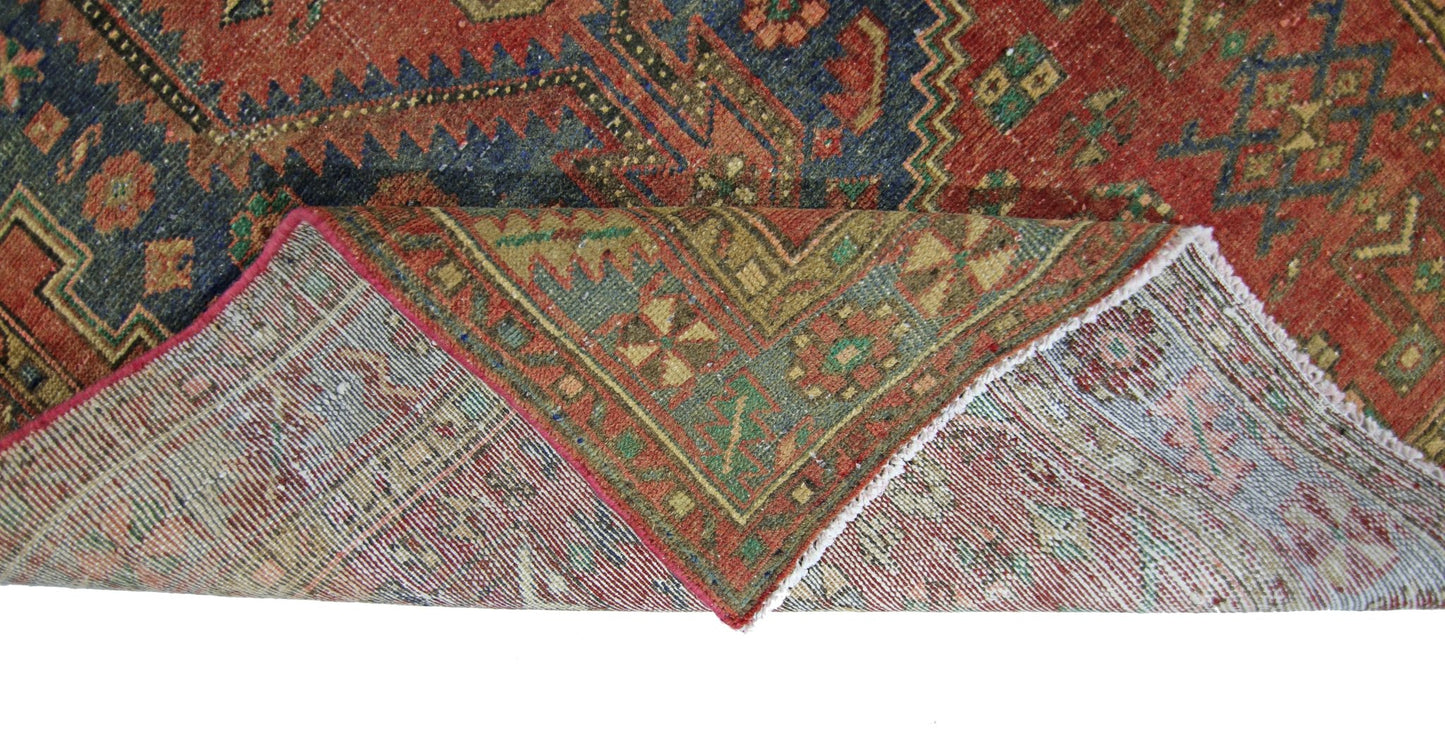 A vintage Persian Hamadan rug with a red and blue geometric pattern, shown folded to reveal its underside.