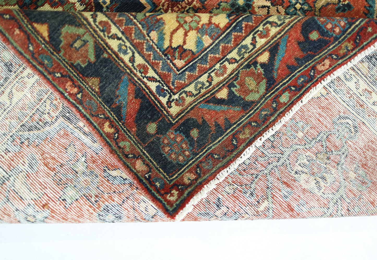 A corner of a vintage Persian rug is folded back to reveal its intricate floral pattern and weave.
