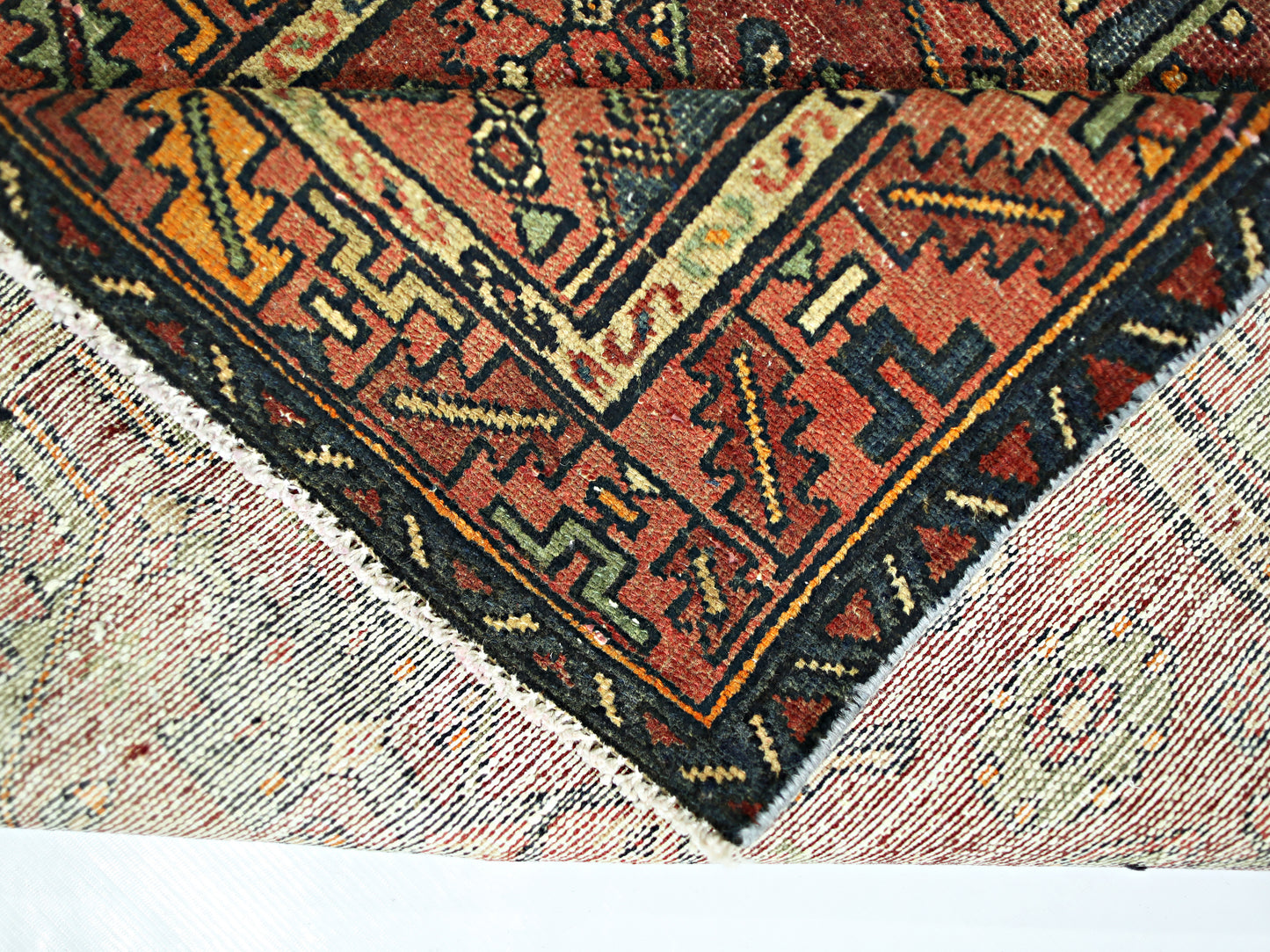 A vintage Persian Hamadan runner with a folded corner showing its wool pile and cotton foundation.