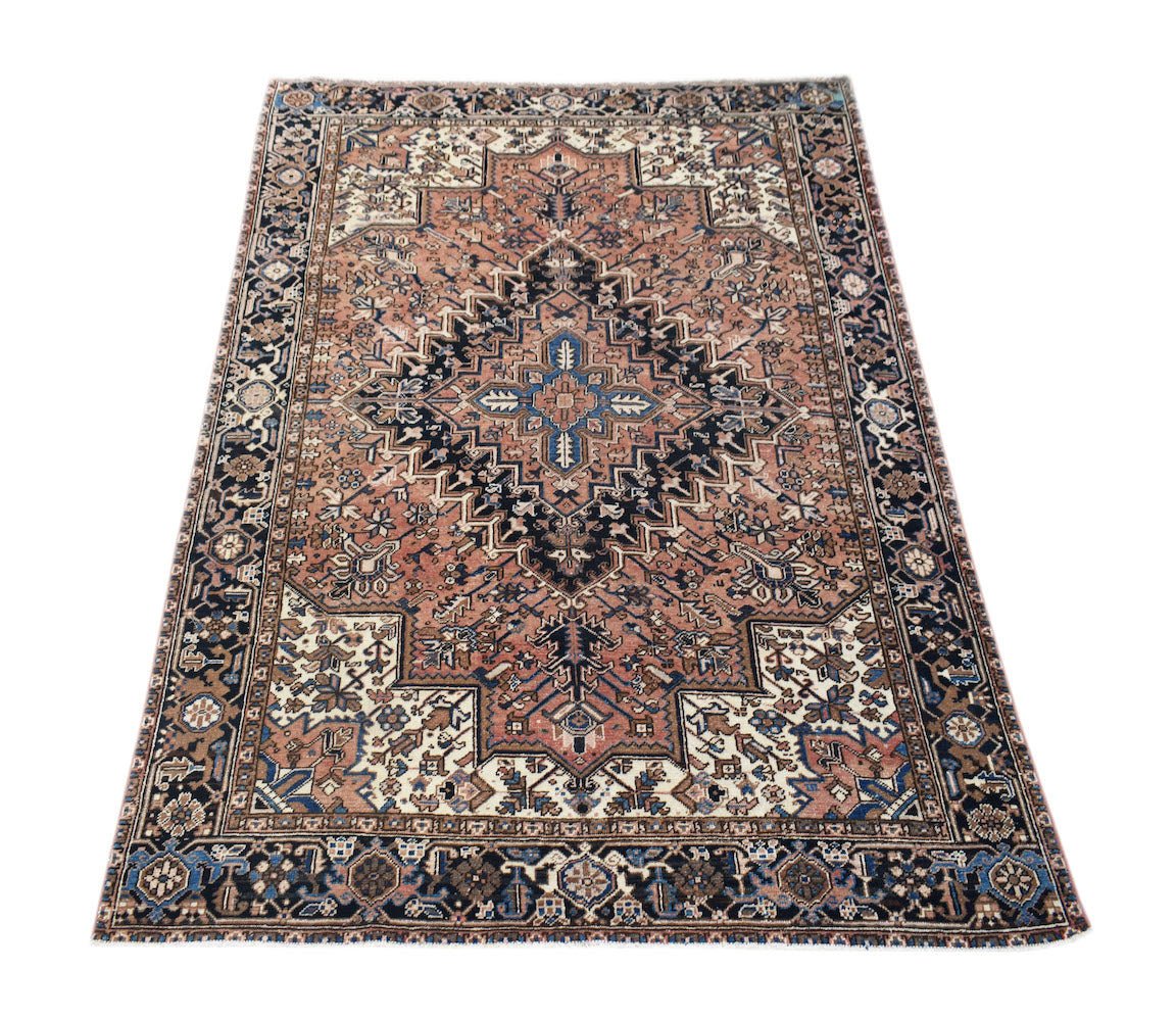 A vintage handwoven Persian Heriz rug featuring a geometric medallion in rust, blue, and cream.