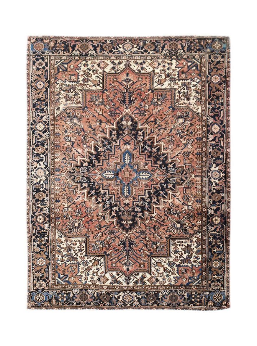 A vintage handwoven Persian Heriz rug featuring a geometric medallion in rust, navy, and cream.