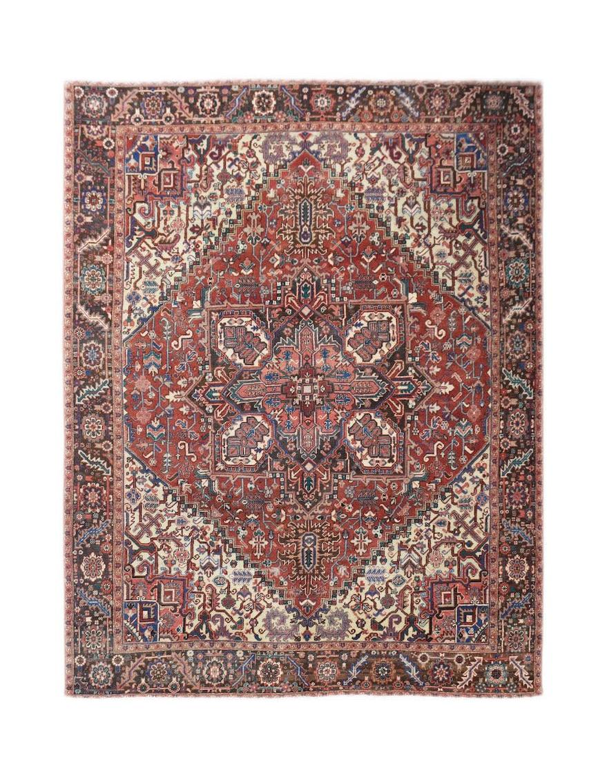 A vintage handwoven Persian Heriz rug featuring a geometric medallion in red, blue, and cream.