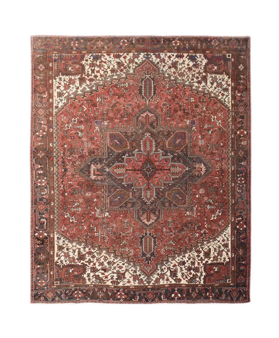 A vintage handwoven Persian Heriz rug featuring a geometric medallion on a rust red field.