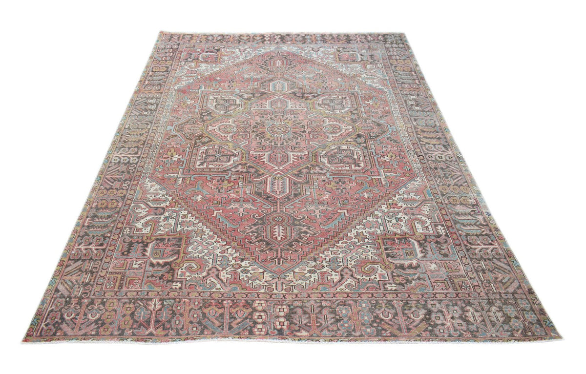 A vintage handwoven Persian Heriz rug featuring a geometric medallion on a faded pink field.