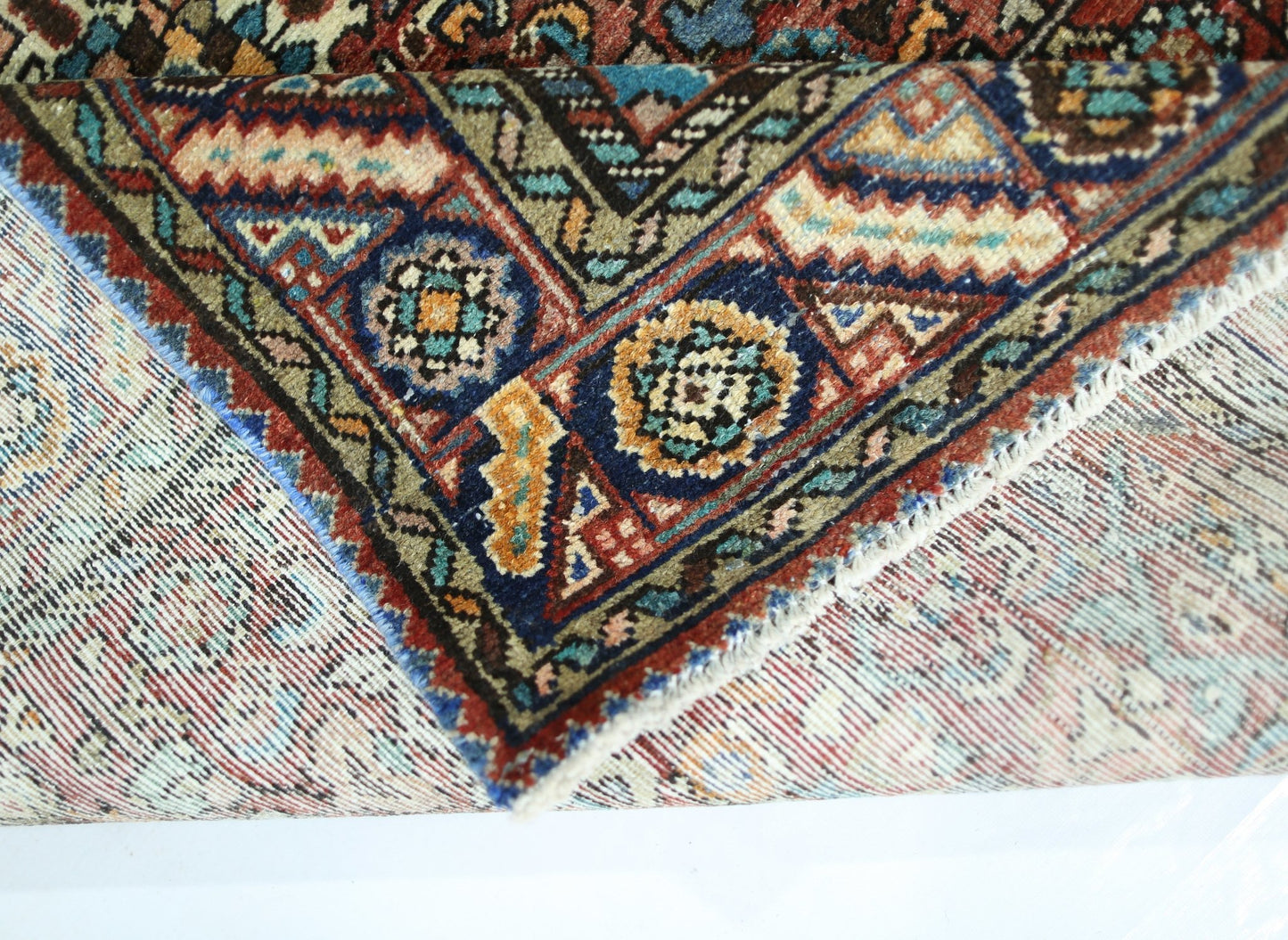 A corner of a vintage handmade Persian rug showing intricate geometric patterns in wool.