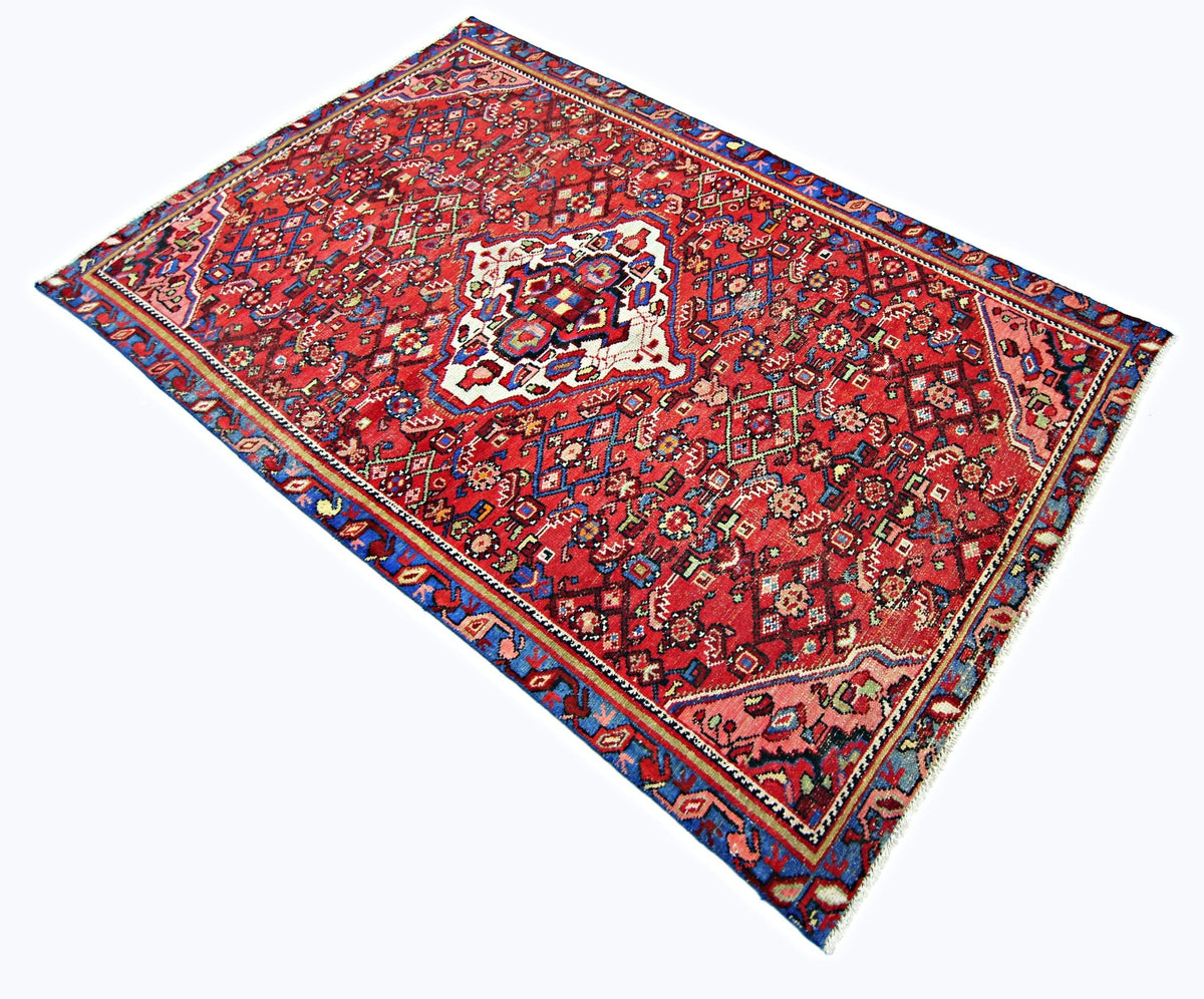 Vintage hand-knotted Persian Hossainabad rug featuring a red field, central medallion, and geometric tribal patterns.