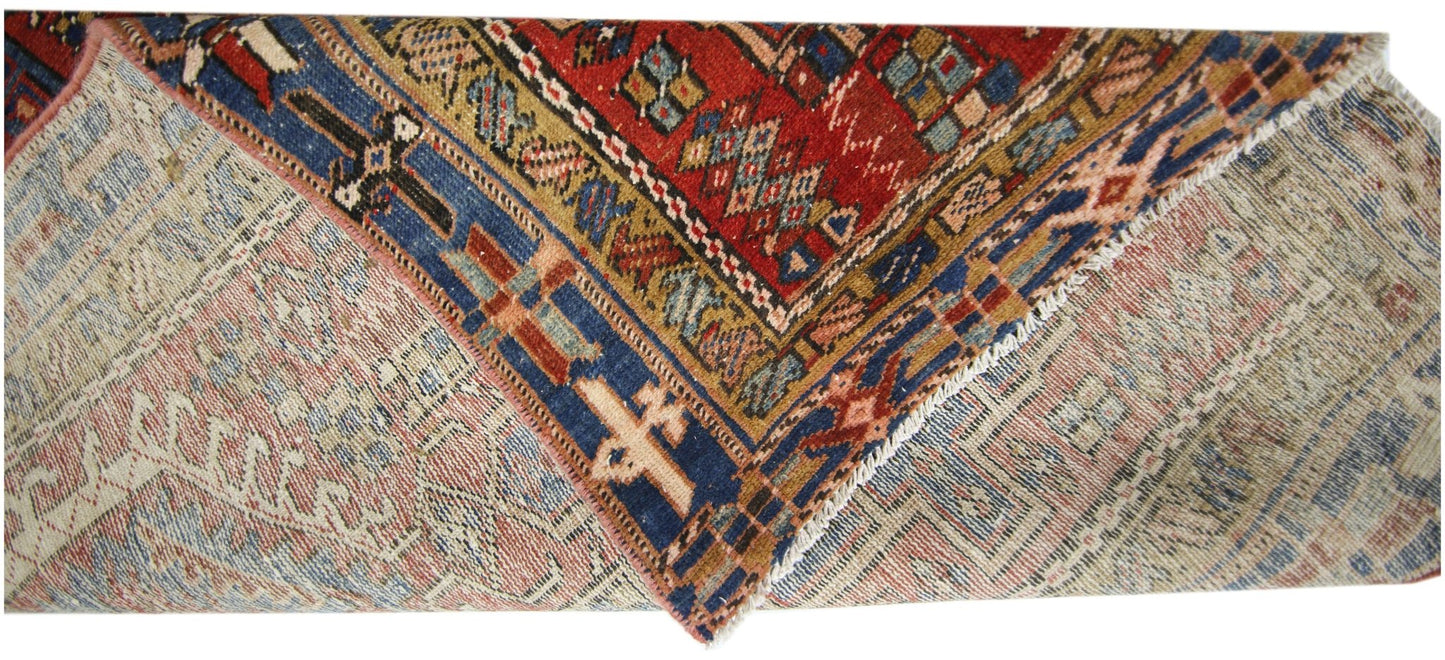 A vintage Persian Karaja runner with a geometric red, blue, and tan wool pattern.