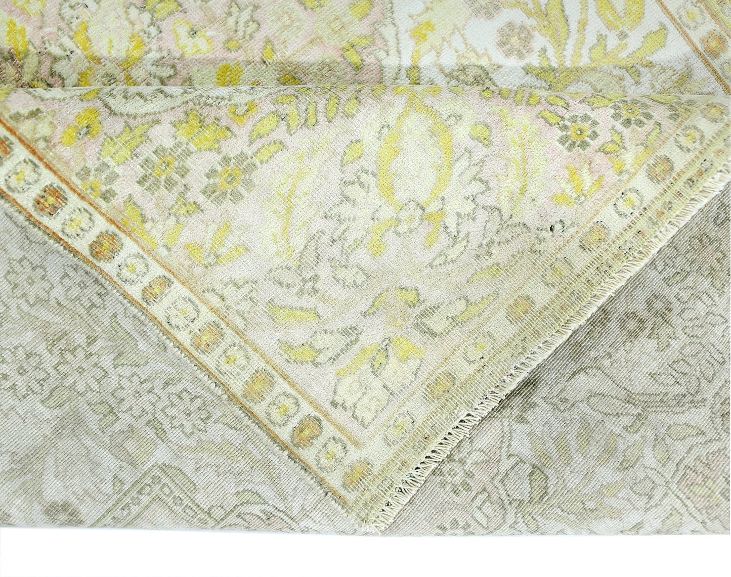A folded vintage Persian Kashan rug featuring a floral pattern in soft yellow and cream tones.