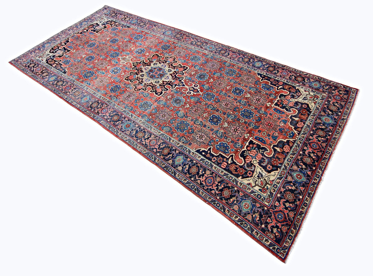 Vintage Persian Kashan runner with a red field, intricate blue floral arabesques, and detailed decorative borders.