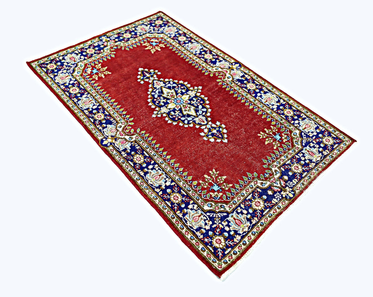 A vintage Persian Kerman rug featuring a central floral medallion on a red field with blue borders.