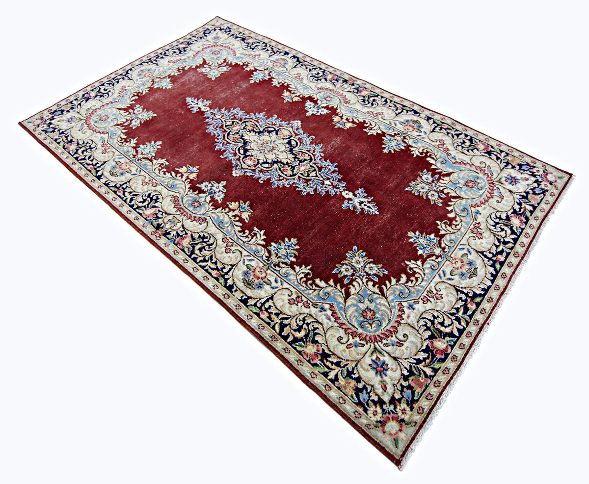 Vintage Persian Kerman rug featuring a deep red field, intricate floral patterns, and a central medallion in blue and cream.
