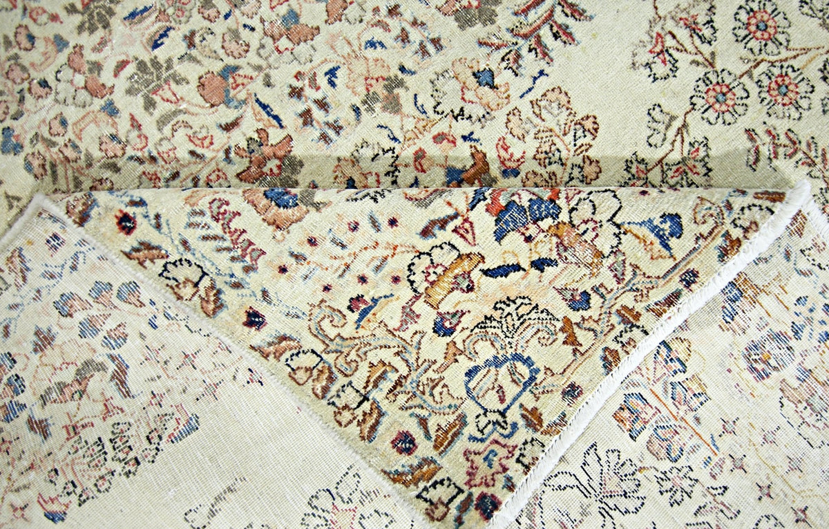 Close-up of a vintage Persian Kerman rug showing intricate floral patterns in blue, red, and cream on a wool pile.