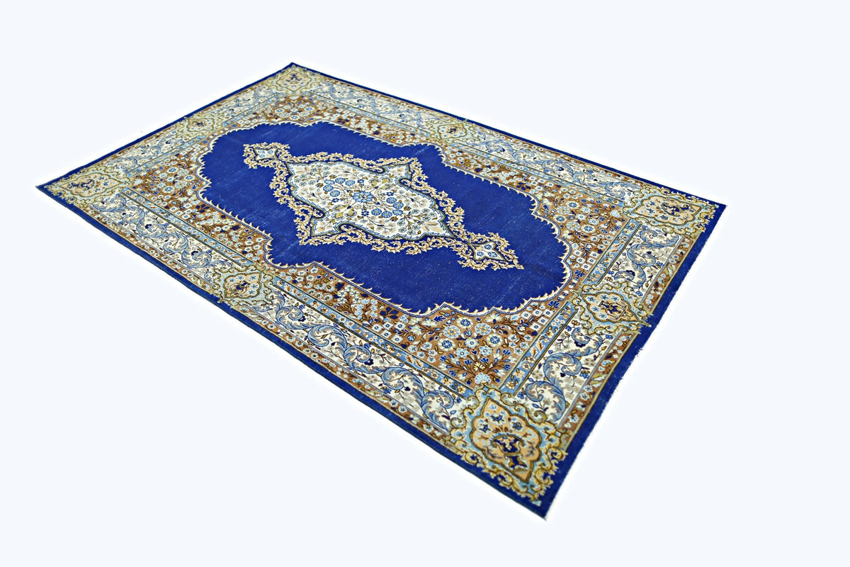 A vintage Persian Kerman rug featuring a central floral medallion on a deep blue field.