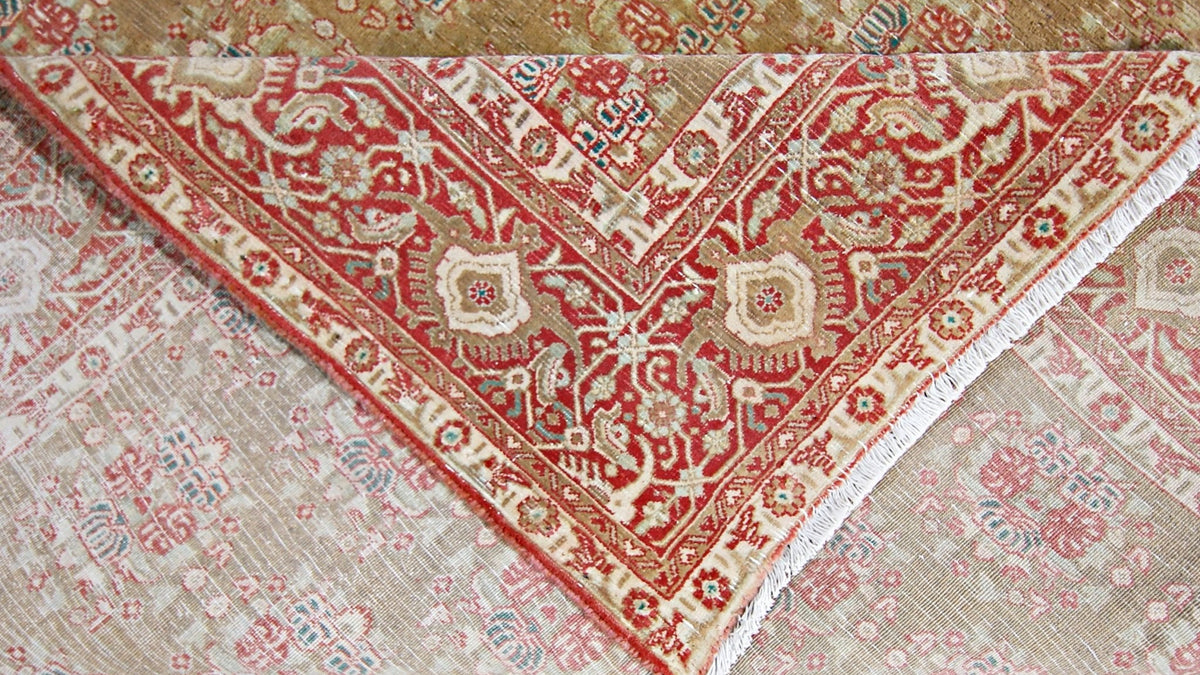 Close-up of a hand-knotted wool Kerman rug featuring intricate red and beige floral patterns with a visible cotton fringe.