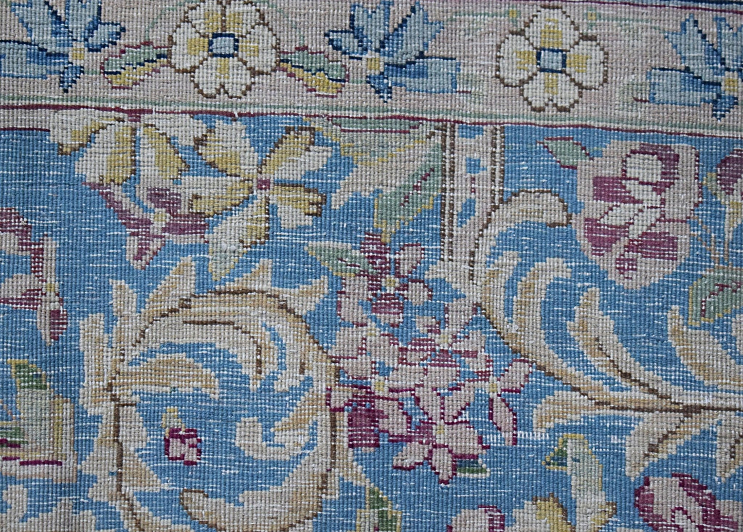 A close-up of a vintage Persian Kerman rug featuring intricate floral patterns on a blue field.