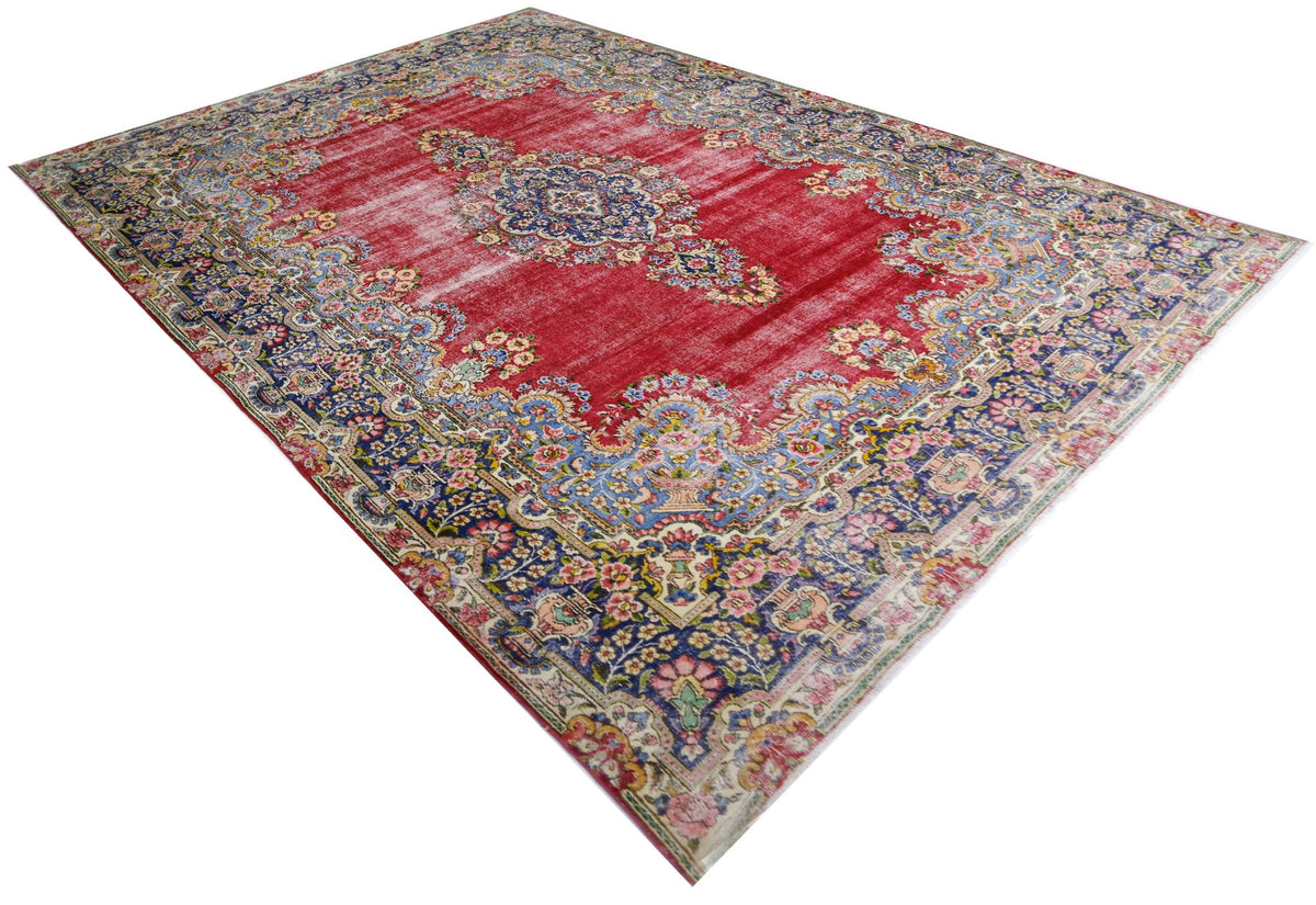 Vintage Persian Kerman rug with a red floral field, central blue medallion, and intricate curvilinear border patterns.