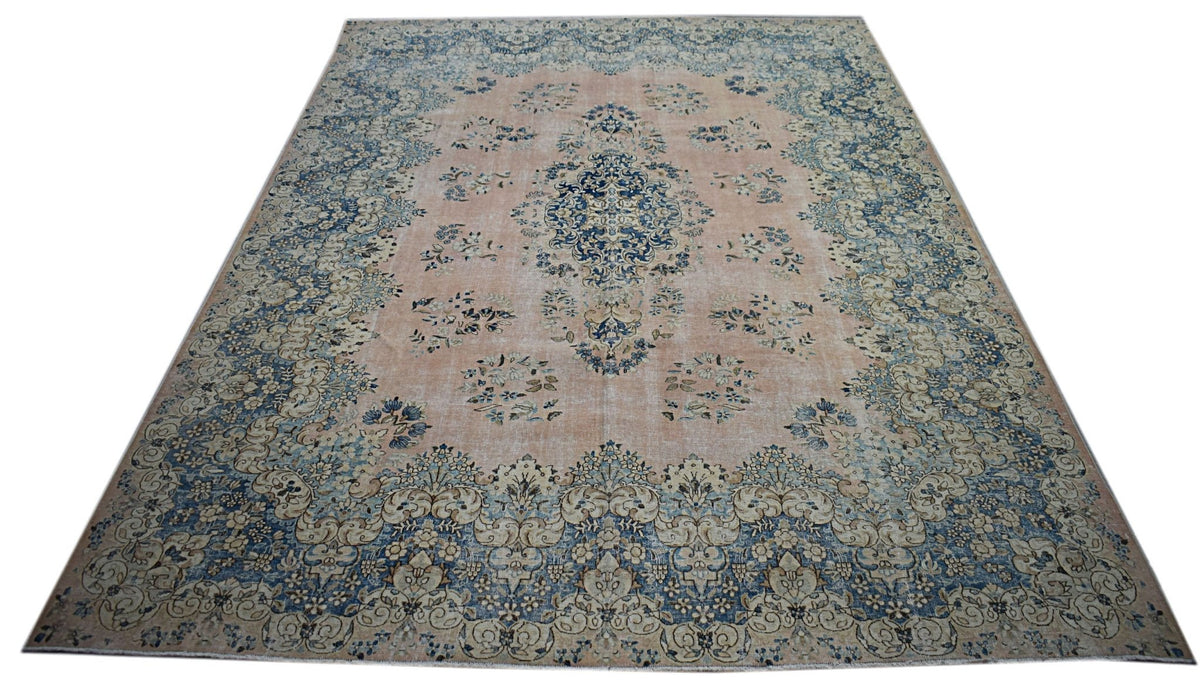 A vintage Persian Kerman rug featuring a central medallion and floral motifs in blue and peach.