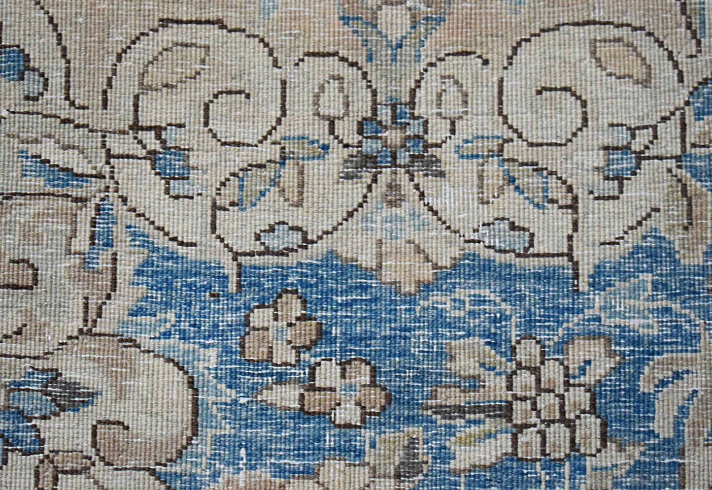 A close-up of a vintage Persian Kerman rug featuring intricate floral patterns in blue and beige.