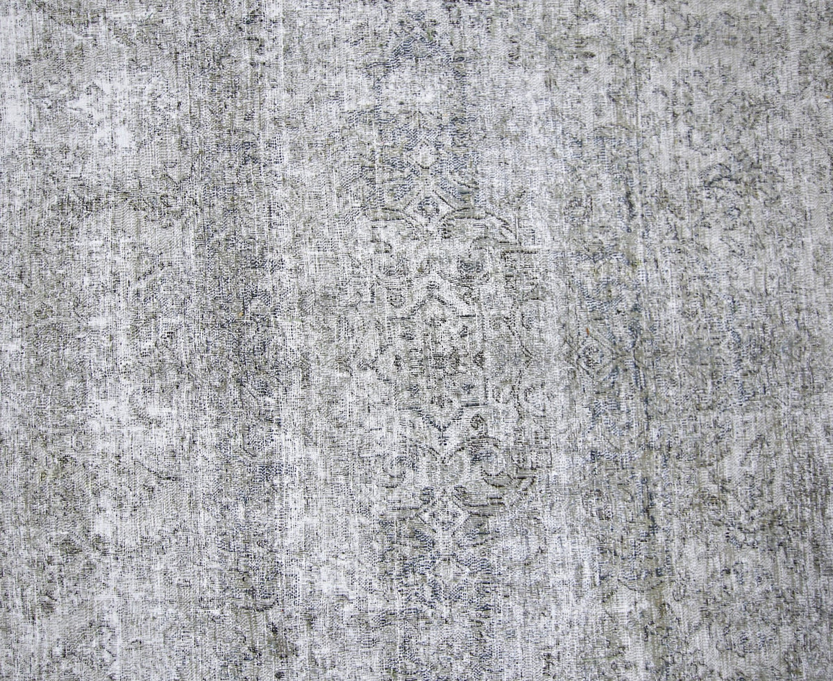 Close-up of a vintage Persian Kerman rug featuring a faded grey and white floral pattern with a low, hand-knotted pile.