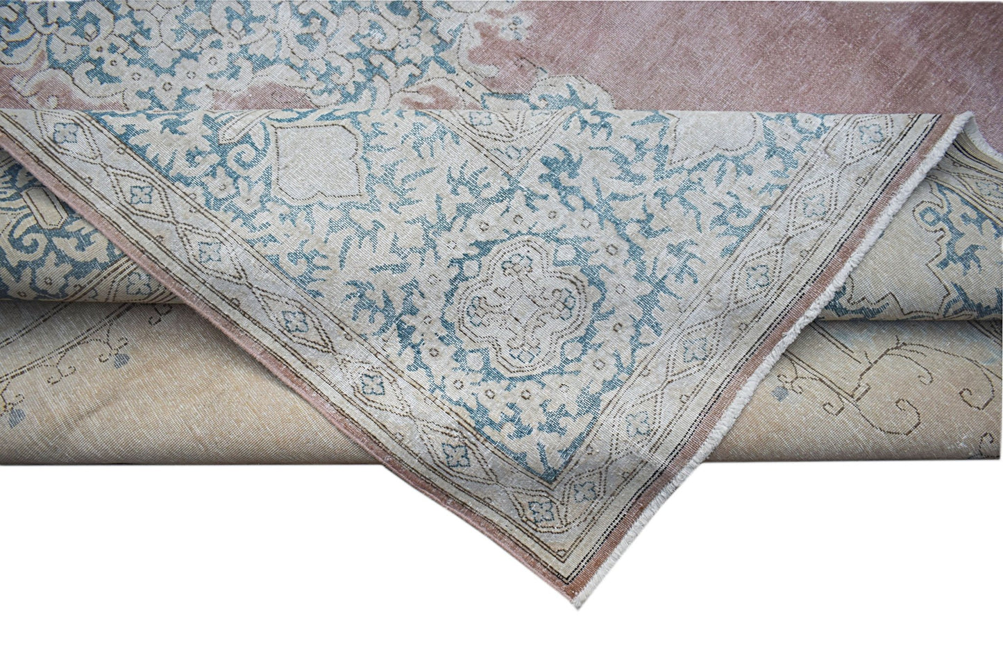 A vintage Persian Kerman rug featuring a blue floral medallion pattern on a soft pink background.