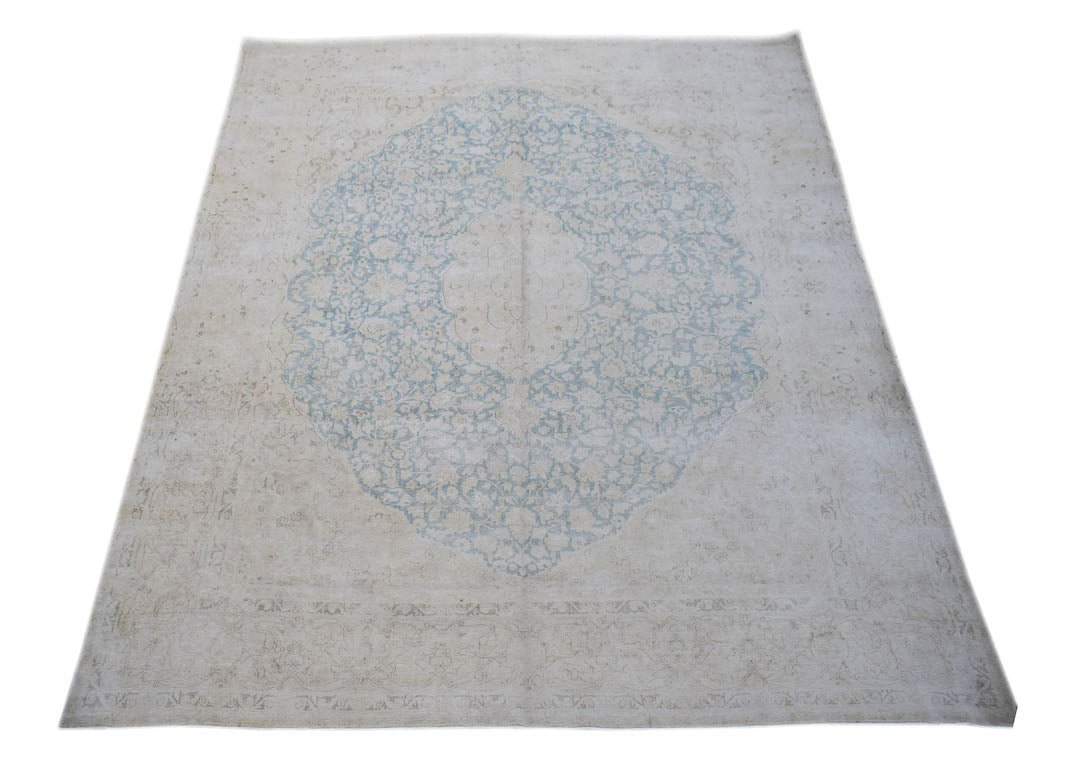 A vintage Persian Kerman rug featuring a central blue floral medallion on a light beige field.