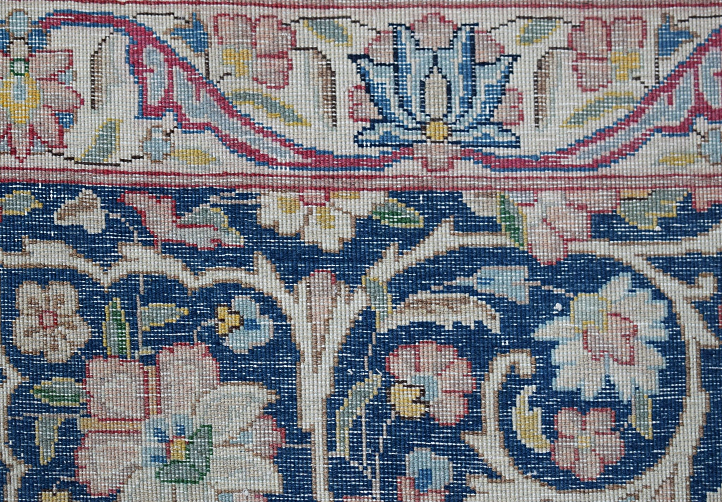 A close-up of a vintage Persian Kerman rug featuring intricate floral patterns on a blue field.