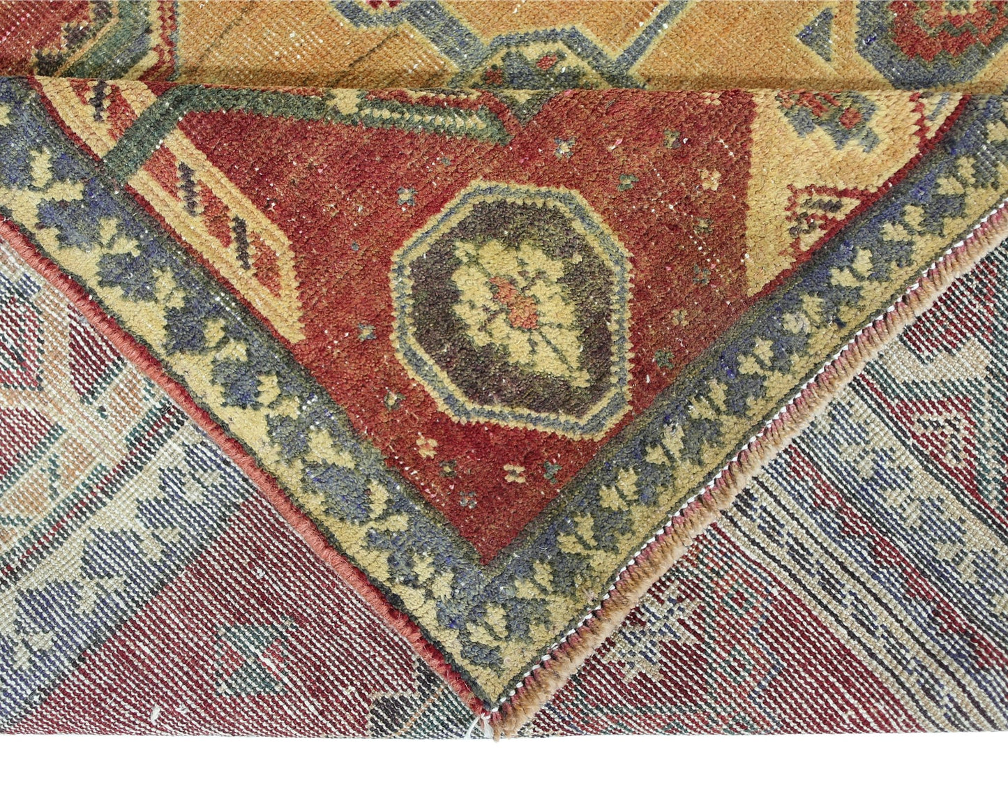 A corner of a vintage Persian rug showing a red field with floral motifs and a blue border.